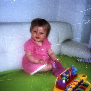 Infant sits on a green blanket with toys.