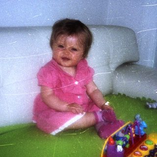 Infant sits on a green blanket with toys.