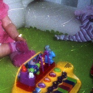 Infant sits on a green blanket with toys.