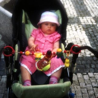 Baby in a stroller with toys, outdoors.