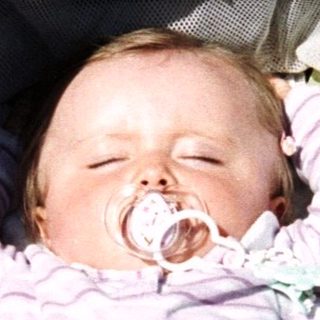 Here's a brief summary of the image: Baby sleeping peacefully in a stroller with a pacifier.
