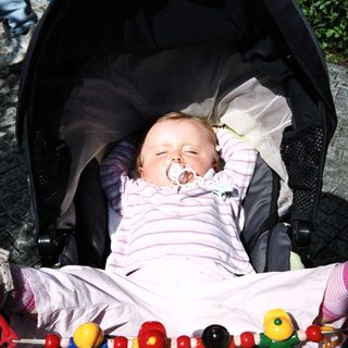 Here's a brief summary of the image: Baby sleeping peacefully in a stroller with a pacifier.