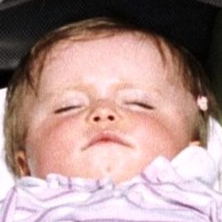 Baby sleeping in a stroller with toys and a bottle.