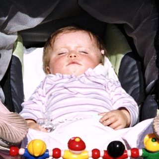 Baby sleeping in a stroller with toys and a bottle.