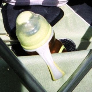 Baby sleeping in a stroller with toys and a bottle.