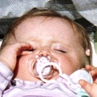 Baby sleeps in stroller with toys and bottle nearby.