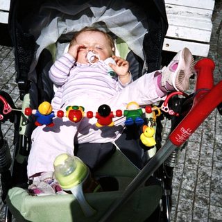 Baby sleeps in stroller with toys and bottle nearby.