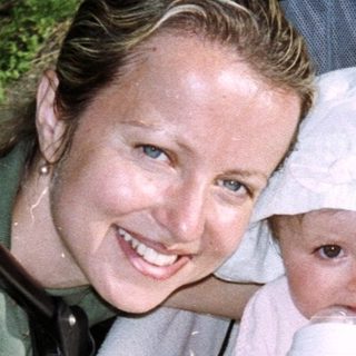 Woman feeds baby in stroller outdoors.