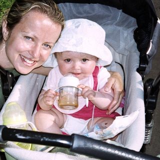 Woman feeds baby in stroller outdoors.