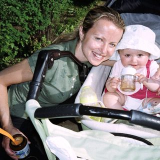 Woman feeds baby in stroller outdoors.
