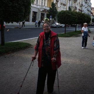 Woman with walking sticks stands in front of a building.