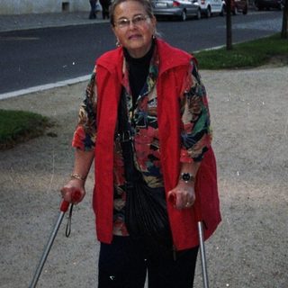 Woman with crutches stands on a street near buildings.