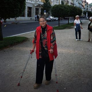 Woman with crutches stands on a street near buildings.