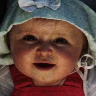 Baby in a stroller sits outdoors looking directly at the camera.