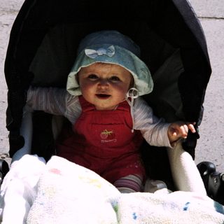 Baby in a stroller sits outdoors looking directly at the camera.
