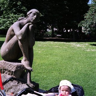 Sculpture, baby in stroller, and green lawn in park.