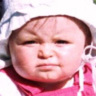 Baby in stroller sits on grass, wearing a hat.