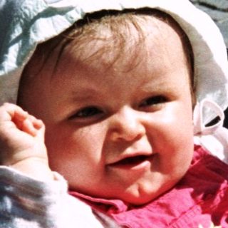 Baby in a stroller, smiling and reaching up.