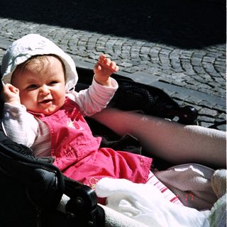Baby in a stroller, smiling and reaching up.