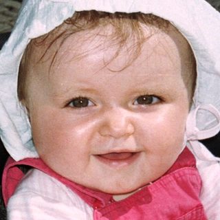 Baby in a stroller, wearing a bonnet and holding a toy.