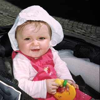 Baby in a stroller, wearing a bonnet and holding a toy.