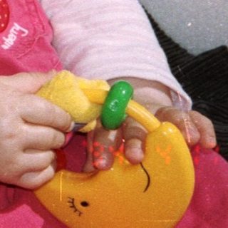 Baby in a stroller, wearing a bonnet and holding a toy.