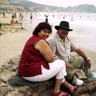Couple relaxes on rocks overlooking a crowded beach.