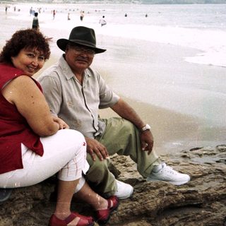 Couple relaxes on rocks overlooking a crowded beach.