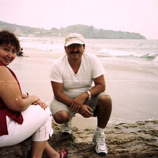 Couple poses on rocks at a crowded beach.