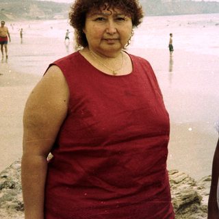 Woman and boy stand on a beach near the ocean.