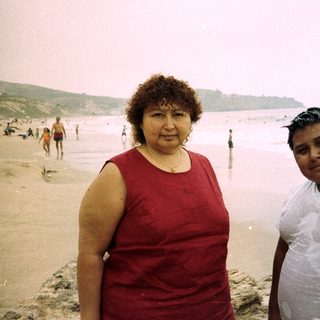 Woman and boy stand on a beach near the ocean.