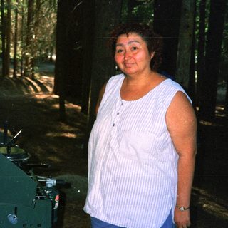 Here's a brief summary of the image: Woman stands near camping gear in a wooded area.