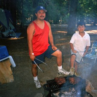 Man grilling food outdoors with a child nearby.