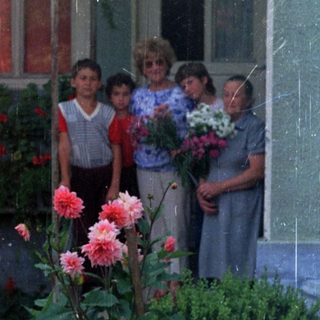 Group of children standing outside a house with flowers.