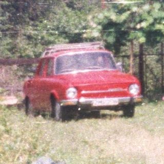 Red car parked near a house with a tiled roof.