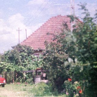 Red car parked near a house with a tiled roof.