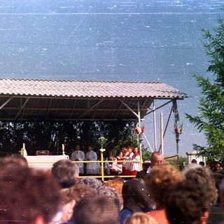 Outdoor ceremony with people gathered under a roofed platform.