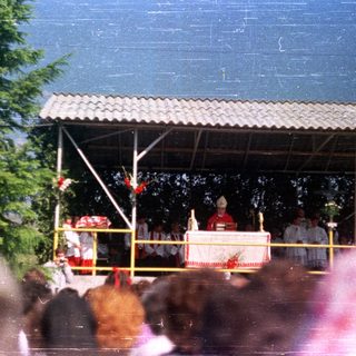 Outdoor religious ceremony with figures on a raised platform.