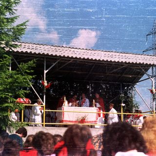 Outdoor religious ceremony with priests and a crowd of people.