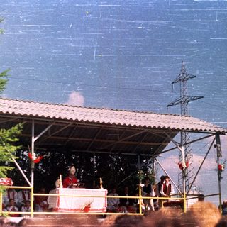 Outdoor religious ceremony with audience and a covered stage.