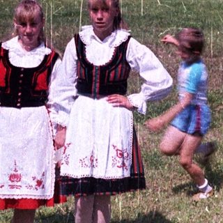 Two girls in traditional dress stand in a grassy field.