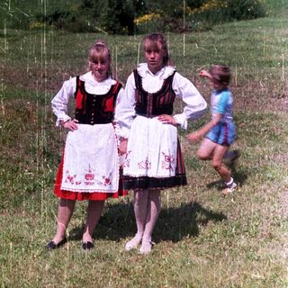 Two girls in traditional dress stand in a grassy field.