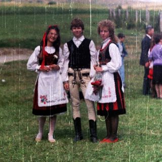 Three people in traditional folk dress stand in a field.