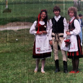 Three people in traditional folk dress stand in a field.