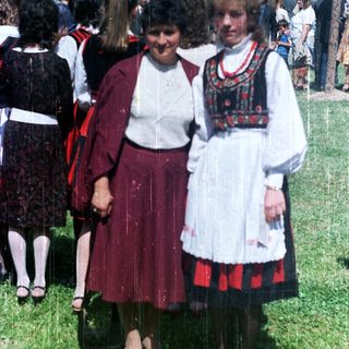 Two women in traditional folk dress stand in a crowd.