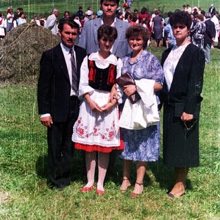 Family posing outdoors amidst a crowd on a grassy field.