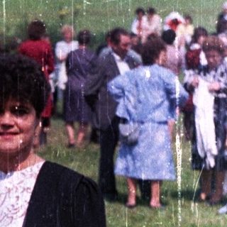 Two women stand in a field during a gathering.