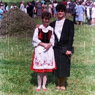 Two women stand in a field during a gathering.