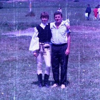 Man and woman in costume stand on a grassy hillside.