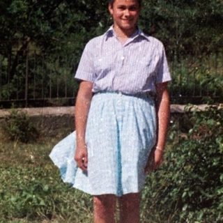 Girl stands on a road with a weeping willow tree.